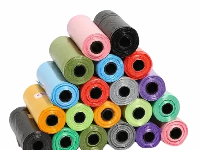 A pyramid stack of colorful rolled dog poop bags, including black, pink, olive green, light blue, orange, red, grey, purple, and teal.